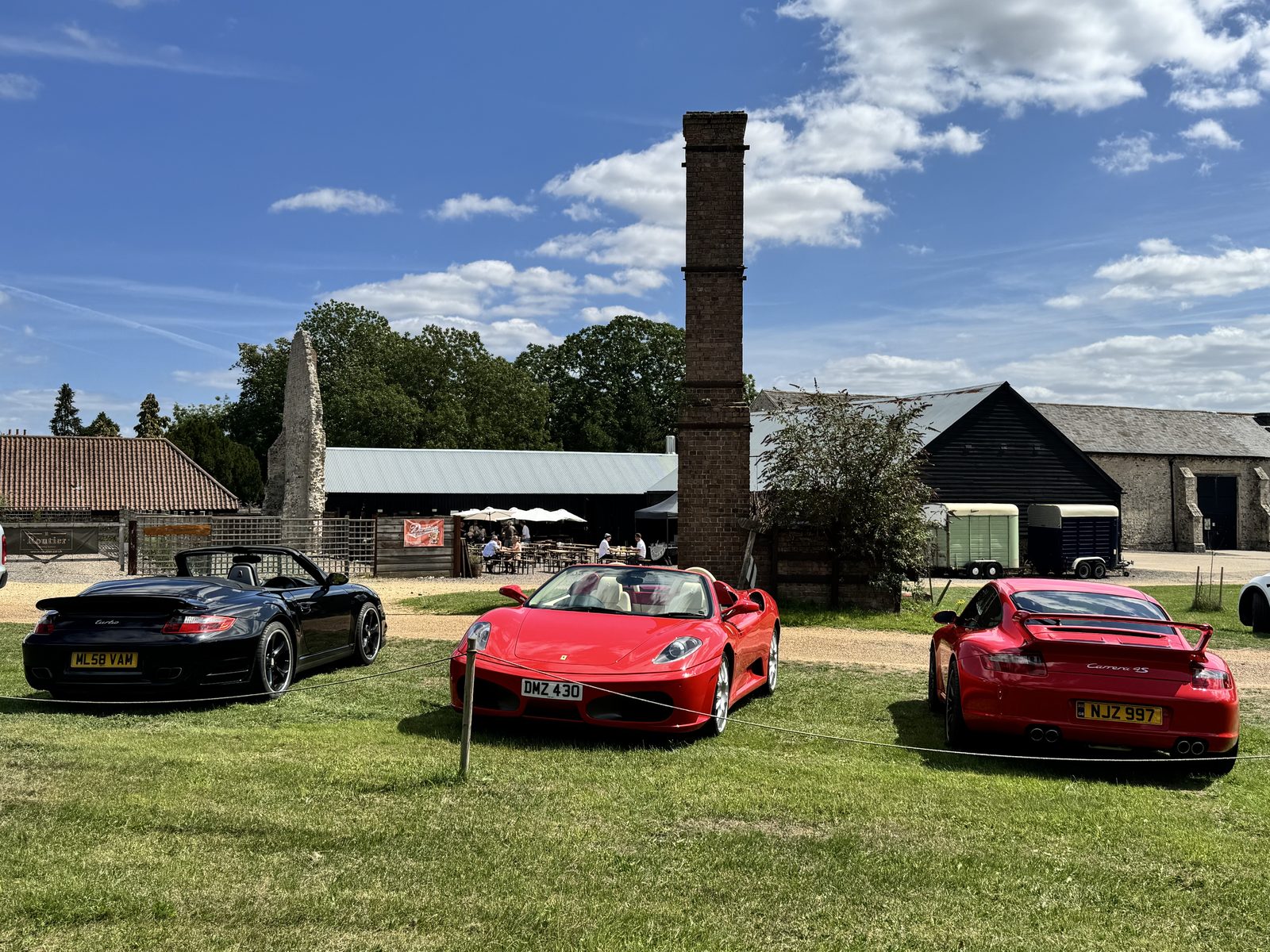 Red F430 Spider parked with a Porsche 997 Turbo Cabriolet and a Carrera at Duration brewery, West Acre